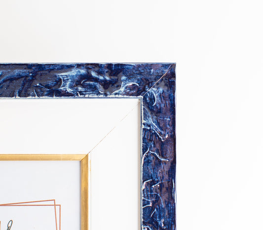 Dettaglio dell'angolo della cornice blu lucido con passepartout in legno bianco e filetto oro